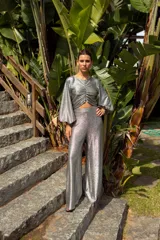 Pantalón de tiro alto confeccionado en tela de lamé plateada con acabado brillante, de corte amplio y ligeramente acampanado.