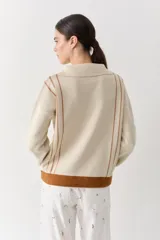 Buzo de punto color beige con rayas verticales marrones, cuello polo con cierre frontal, puños y ruedo acanalados en color marrón. Incluye cordones amarillos ajustables en la cintura.