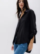 Camisa de corte suelto y textura fluida, confeccionada en viscosa sostenible. Presenta cuello clásico, cierre frontal de botones y mangas largas con detalle de trabilla para enrollar.