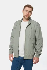 Campera liviana de color verde grisáceo, con cierre frontal, cuello alto y puños elásticos. Presenta un pequeño parche con logo en el pecho.