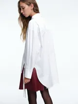 Camisa blanca de algodón con cuello clásico, cierre frontal de botones y diseño de paneles verticales. Presenta tiras largas irregulares en el frente que aportan movimiento y un estilo contemporáneo.