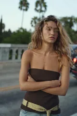 Top palabra de honor color marrón oscuro, con escote recto y hombros descubiertos. Incluye un cinturón en forma de corbata con estampado geométrico en tonos beige y blanco, que se anuda en la parte frontal. Cierre lateral con cremallera oculta.