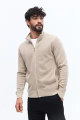 Campera de algodón color beige, estilo deportivo con cierre frontal, cuello alto y puños. Presenta bolsillos laterales y un pequeño logo bordado en el pecho.