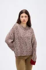 Sweater de tejido de punto con efecto jaspeado, corte holgado y cuello redondo. Presenta mangas largas con puños en contraste de color, uno en tono oscuro y otro en tono rojizo.