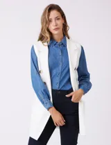 Chaleco largo tejido color blanco de la marca Sioni, con cuello solapa, doble botonadura dorada en el frente y bolsillos aplicados.