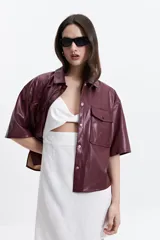 Camisa de manga corta confeccionada en cuero sintético color bordó, con cuello clásico, cierre frontal de botones metálicos y dos bolsillos frontales con solapa.