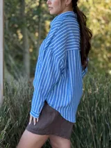 Camisa celeste con rayas verticales blancas, de manga larga, cuello camisero y cierre frontal con botones.