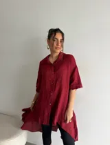 Camisola de lino color beige, de corte amplio, con cierre frontal de botones y diseño asimétrico más largo en la parte trasera.