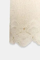 Falda midi de tejido rústico en color beige, con tiro medio, cintura elástica y detalle de aplicación de crochet en el bajo.