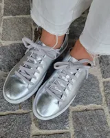 Zapatillas plateadas de cuero con cordones grises y suela blanca.