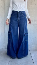 Pantalón tipo jean cargo de corte ancho y tiro alto, confeccionado en denim azul oscuro. Presenta bolsillos laterales tipo cargo con solapa y costuras reforzadas a lo largo de las piernas.