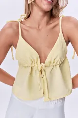 Top amarillo pálido con escote en V, breteles finos con lazos en los hombros y corte holgado con frunce y lazo ajustable en el centro del busto.