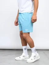 Bermuda de felpa color celeste, con cintura elástica y cordón de ajuste. Presenta el logo Umbro bordado en la pierna izquierda.
