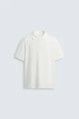 Polo de manga corta color blanco roto, con cuello solapa y cierre frontal de cremallera. Presenta un tejido de piqué estructurado y corte regular fit.