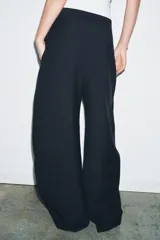 Pantalón de tiro medio con diseño wide leg, confeccionado en mezcla de lyocell. Presenta detalle de pinzas en el delantero, cierre frontal con cremallera, botón y ganchos metálicos.