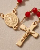 Collar rosario de acero con baño de oro, compuesto por cuentas de cristal rojo y un dije de San Benito con cruz colgante.