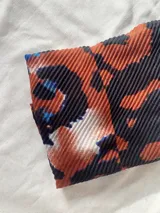 Pañuelo rectangular de textura plisada con estampado abstracto en tonos tierra, negro y azul.