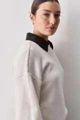 Sweater negro de tejido suave con escote redondo, mangas largas y calce relajado, con terminaciones acanaladas en cuello, puños y ruedo.