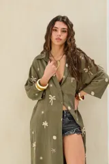 Camisola larga color verde militar con bordados de palmeras y soles en hilo crudo, cuello camisero, mangas largas y bolsillo frontal.