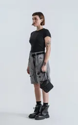 Bermuda cargo color gris oscuro (carbón), de corte recto y largo hasta la rodilla, con cinturón de cinta negra ajustable con hebilla de plástico. Presenta bolsillos laterales y bolsillos cargo con solapa en las piernas.