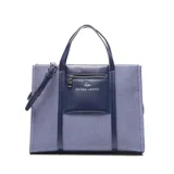 Cartera grande tipo tote bag de textura denim con detalles en cuero sintético azul oscuro. Cuenta con doble asa de mano, correa ajustable para el hombro y un bolsillo frontal con cierre y el logo de la marca Extra Large.