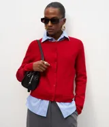 Cardigan de punto color rojo, con mangas largas, cierre frontal con botones y bolsillos delanteros. Presenta acabado acanalado en el escote y los puños.