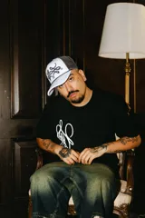 Gorra trucker gris con paneles frontales blancos y paneles traseros de rejilla negra. Presenta un logo bordado en el panel frontal y una cuerda decorativa en la base de la corona.