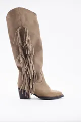 Bota bucanera de cuero vacuno color beige, con diseño de caña alta y detalle de flecos largos laterales. Posee taco cuadrado y punta redondeada.