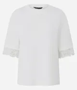 Remera de algodón blanca de corte recto y holgado, con cuello redondo y mangas cortas amplias que presentan una delicada aplicación de encaje en los dobladillos.