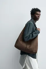 Bolso de hombro marrón con efecto serraje. Tiene un compartimento principal con cierre magnético y un bolsillo interior con cremallera. El asa es del mismo material.