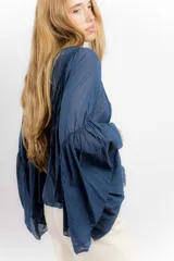 Camisa de algodón con diseño romántico, mangas amplias y detalles de puntillas verticales en el frente. Presenta un corte holgado y fluido.