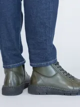 Botín de cuero color verde oscuro con sistema de ajuste mediante cordones negros y suela de poliuretano flexible. Presenta una caña de 10 cm y un taco de 3 cm, ofreciendo un diseño ergonómico y confortable para el uso diario.