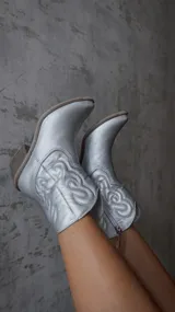 Botas texanas de caña corta en color plateado metalizado, con diseño de costuras decorativas en el lateral y taco cuadrado de madera.