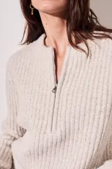 Sweater de punto color crema, con cuello redondo y cierre metálico a la mitad del frente.