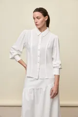 Camisa blanca de manga larga con cuello clásico, botonadura frontal y puños anchos.