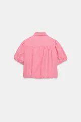 Camisa corta de cuello solapa y manga corta abullonada acabada en elástico, color verde con estampado de cuadros vichy. Cuenta con un bolsillo de plastrón en el delantero, bajo con elástico y cierre frontal con botones.