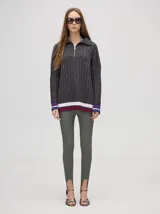 Pullover de algodón color beige, con tejido en ochos, cuello polo con cierre frontal y puños a rayas de colores (blanco, bordó y amarillo). El diseño es holgado y cae por debajo de la cadera.