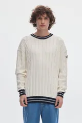 Buzo de punto blanco crudo con tejido de ochos y diseño regular. Cuenta con cuello redondo, puños y ruedo acanalados en color negro con líneas blancas en contraste.
