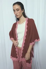 Poncho marrón con detalles de bordes ondulados en color rosado, confeccionado en mezcla de acrílico, poliéster y elastano, de diseño abierto y mangas amplias.