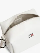 Cartera bandolera blanca Tommy Jeans de poliuretano, diseño cuadrado con cierre de cremallera y compartimento principal. Cuenta con correa ajustable, insignia metálica con el logo de la marca en el frente y un colgante lateral extraíble de cordón rojo trenzado con argollas metálicas.