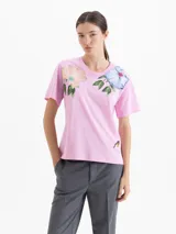 Remera de algodón con cuello redondo y mangas cortas. Presenta un diseño estampado con flores grandes en la parte superior delantera y un pequeño detalle bordado en la parte inferior.