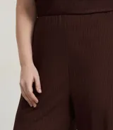 Pantalón de tiro alto, corte flare (acampanado), color marrón oscuro, confeccionado en tejido texturizado anarruga con cintura elástica.