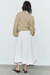 Falda midi blanca de tiro medio con bolsillos delanteros y bajo asimétrico. Cierre lateral con cremallera oculta.