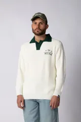 Sweater de punto con textura waffle en color blanco, con cuello polo en contraste color verde oscuro y cierre frontal de botones. Presenta un bordado decorativo en el pecho y un corte relajado.