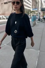 Pantalón de vestir marrón oscuro, tiro alto, con pernera ancha y pinzas frontales. Presenta un bolsillo con tapeta en la parte superior delantera.