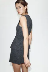 Vestido midi de cuello redondo y sin mangas, confeccionado en tejido con textura. Presenta un diseño que simula dos piezas, con un cinturón integrado a tono y cierre frontal mediante botones forrados.
