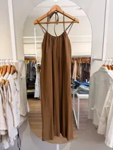 Vestido largo marrón de silueta amplia y caída fluida, con escote fruncido y tiritas finas ajustables al cuello.
