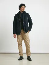 Campera de abrigo color verde militar, con capucha desmontable forrada, cierre frontal con cremallera y botones a presión. Cuenta con múltiples bolsillos: dos en el pecho con cierre, dos en la cintura con botones y un bolsillo en la manga. El interior está forrado para mayor calidez.