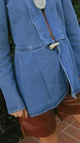 Blazer de denim azul con corte a la cintura, mangas largas con hombros ligeramente abullonados y cierre frontal mediante un botón de guampa.