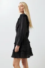 Vestido corto negro con escote en V, mangas largas abullonadas con puños elásticos, falda con volados y cinturón trenzado.